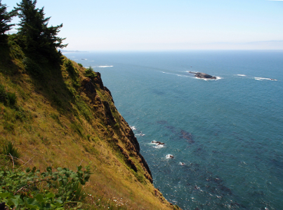 [Looking over the edge of a very sharp drop to the water below. There are whitecaps around several small rocks which are just above the water line. A much larger rock a bit further from shore is the one named Gull Rock.]